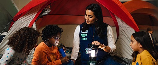 Camp_027_530X220 Troop leader with Girl Scouts in a tent outdoors