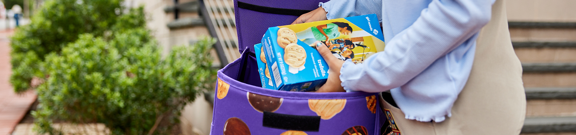 girl scout wearing uniform sash putting trefoil girl scout cookie boxes into cookie transport bag 