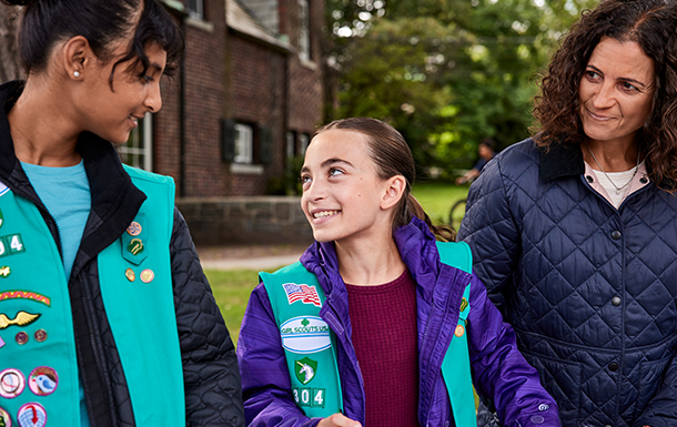 volunteer with junior girl scouts at outside cookie booth smiling